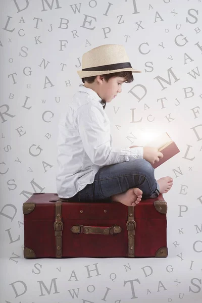 Хлопчик читає книжку, що сидить у валізі. Композитне зображення хлопчика читати книгу — стокове фото
