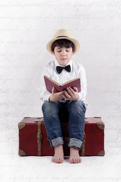 Fiú ül egy bőrönd olvasott. Kompozit kép fiú olvasni egy könyvet — Stock Fotó