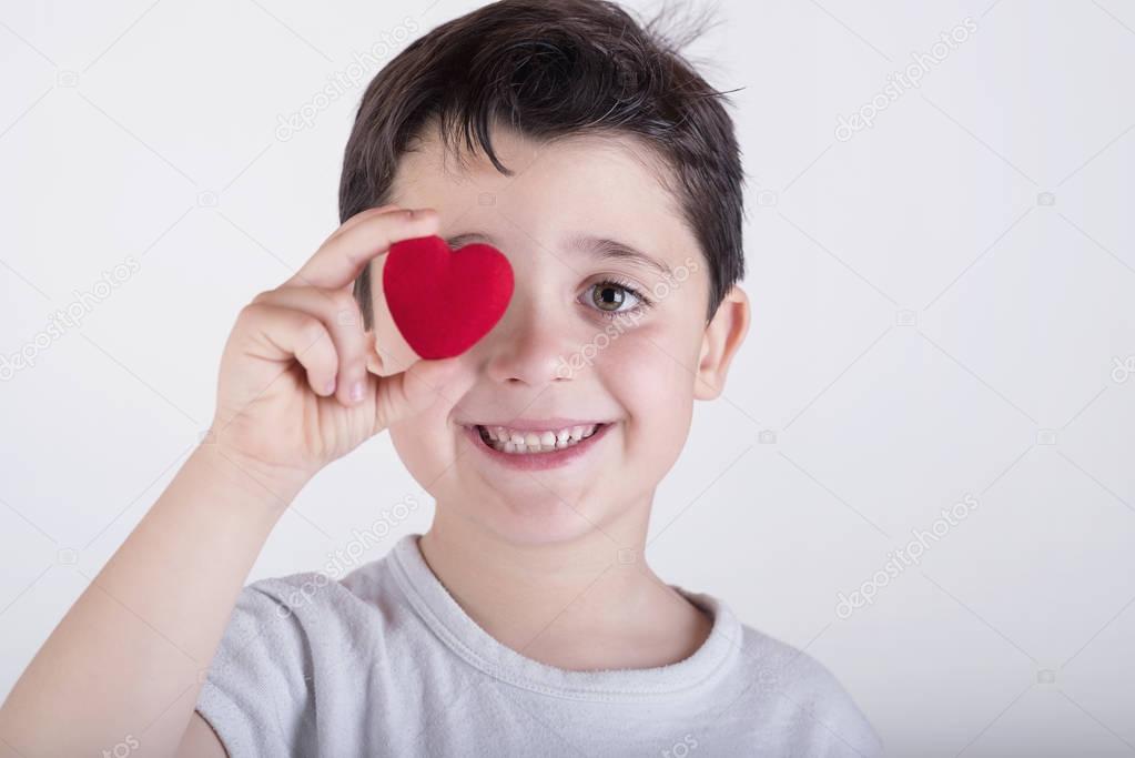 Playful little boy covering her eye with heart