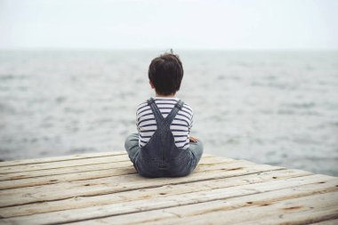 Düşünceli çocuk liman bölgesinde otur. Arkadan Görünüm