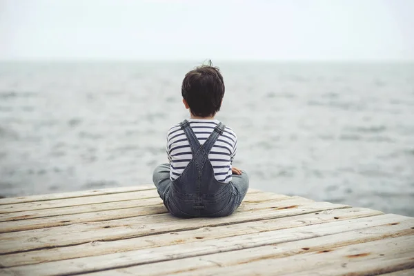 Promyšlené dítě sedět na nábřeží. Pohled zezadu — Stock fotografie