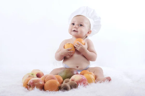 Pequeno bebê feliz no chapéu de um chef com frutas — Fotografia de Stock