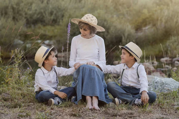 Grootmoeder met haar kleinkinderen zitten in het veld — Stockfoto