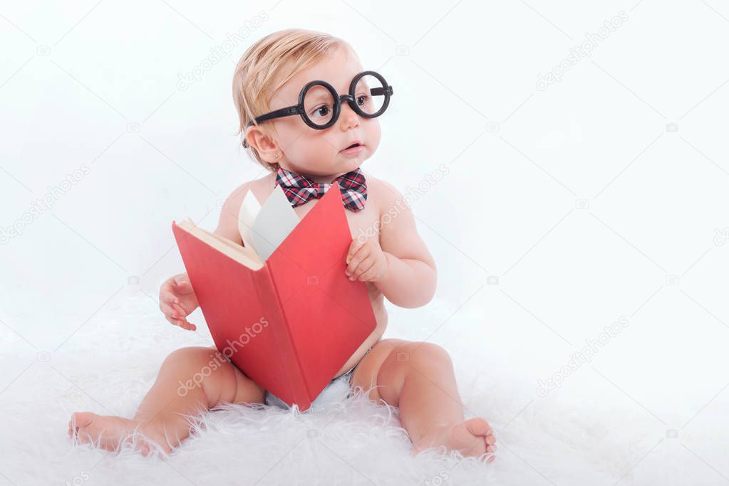 Little happy baby reading a book with glasses and tie