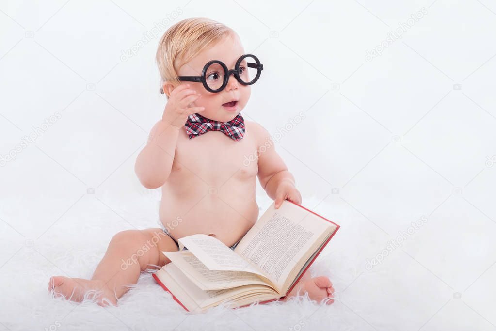 Little happy baby reading a book with glasses and tie