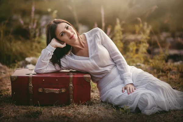 Woman sitting in the field with suitcase — Stock Photo, Image