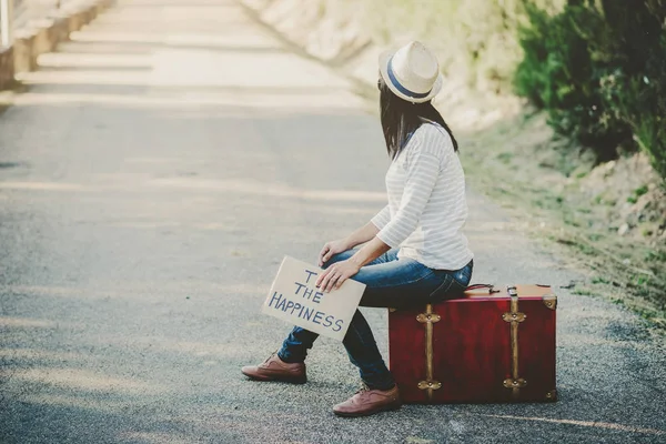 Mladá žena sedící na kufru na silnici — Stock fotografie