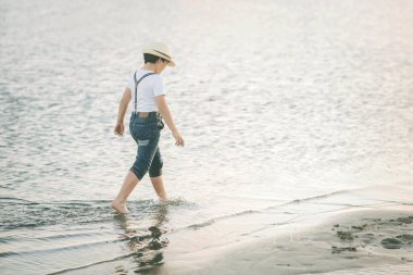 Çocuk dışarıda sahilde yürüyor.
