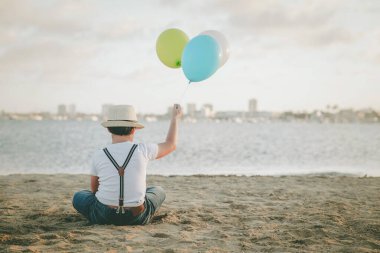 Kumsalda renkli balonları olan küçük bir çocuk.