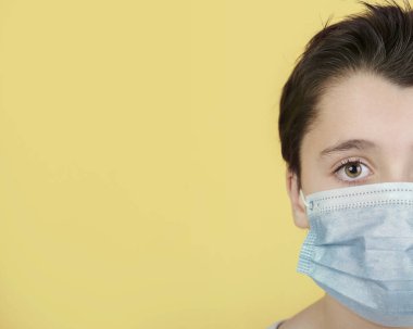 Coronavirus, sarı arka planda tıbbi maske takan çocuğun yakın çekimi.