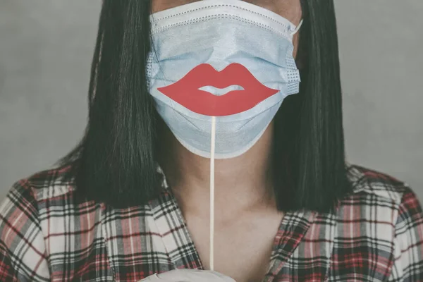 woman wearing medical mask and lips false on stick over gray background