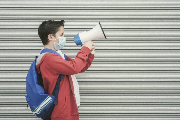 kid with medical mask and backpack screaming with megaphone back to school outdoor