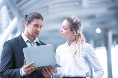 Ofis dışında yürüyen ve konuşan iki iş arkadaşı, bir kağıt ya da dizüstü bilgisayarla bir projeyi tartışıyorlar.