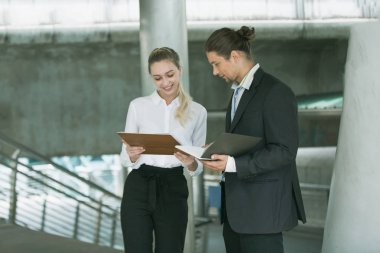 Ofis dışında yürüyen ve konuşan iki iş arkadaşı, bir kağıt ya da dizüstü bilgisayarla bir projeyi tartışıyorlar.