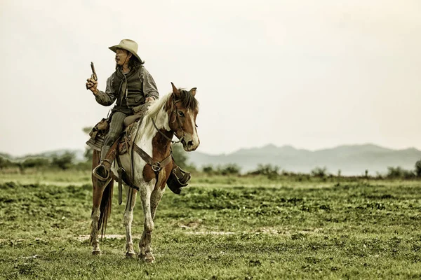 cowboy and horse at first light,mountain, river and lifestyle with natural light background. cowboy riding horse with hand holding gun against sunset.