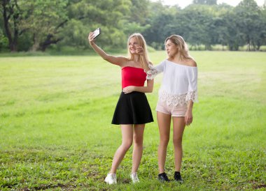 Parkta güneşlenen genç kadınlar selfie çekiyorlar. 