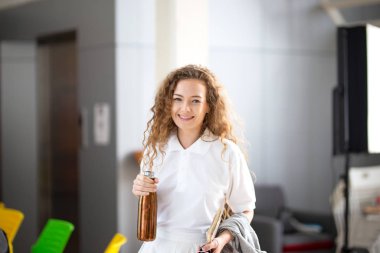 Beyaz kadın gömleği, sarı saçlı, şişede su içen.