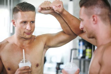 Beyaz tenli yakışıklı bir genç adam ve spor salonundaki egzersiz dersinde aynadan yansıyan bardakla tişörtsüz ve kaslı bir adam. Sağlıklı spor yaşam tarzı, spor konsepti. Metnin için kopyalama alanı ile.