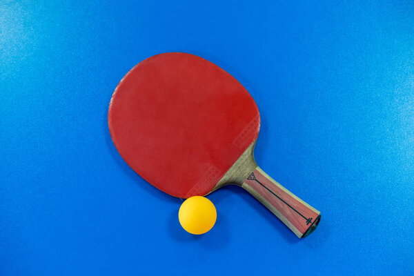 Ping pong paddle with orange ball on blue table