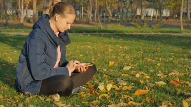 Fille automne dans le parc se trouve sur l'herbe, l'envoi de sms du téléphone . — Video