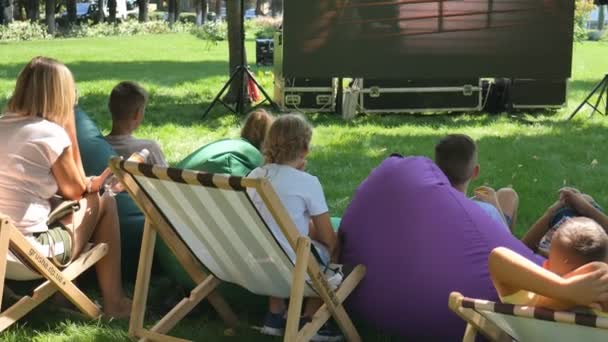 Ucrania, Kirovograd-julio 2019. Mucha gente se sienta en el césped en un parque público y ve una película, dibujos animados. Festival callejero. Mostrando una película al aire libre. Niños en el evento callejero . — Vídeo de stock