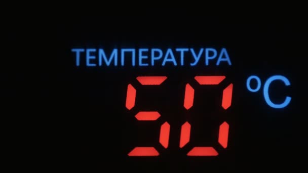 Digital termometer med röda siffror visar temperaturökningen i celsius mot svart bakgrund. Inskrift på ryska - "Temperatur". — Stockvideo