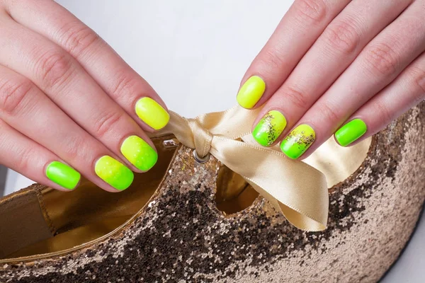 Woman with green and yellow manicured nails holding a gold high heel.