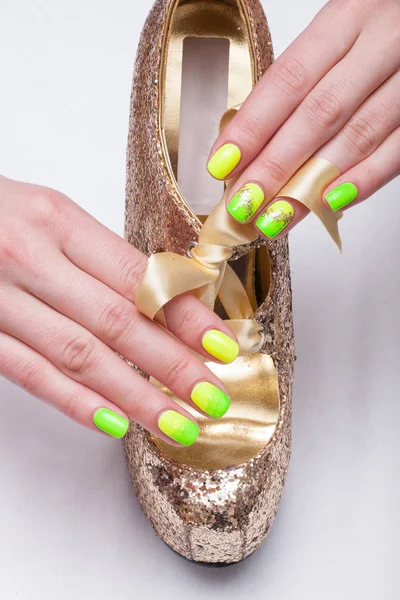 Woman with green and yellow manicured nails holding a gold high heel.