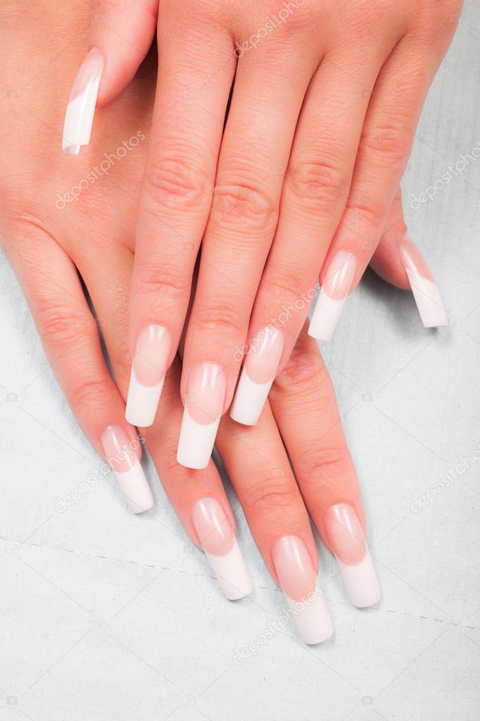 Closeup of hands of a young woman with french manicure on nails against white background