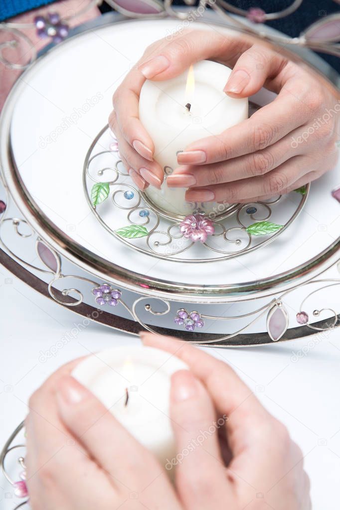 Female hands with beautiful manicure hold a candle.