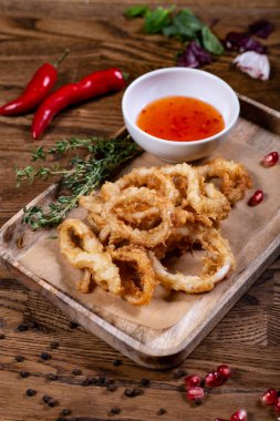 Tahtada acı biber soslu kızarmış soğan halkaları.