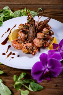 Beyaz tabakta haşlanmış karides ve ahşap masada mor bir orkide.
