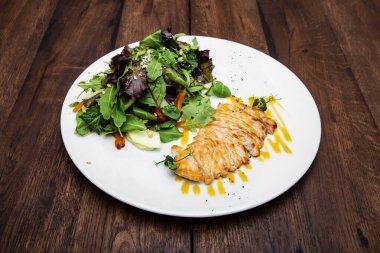 Izgara tavuk göğsü ve salata, marul ve hardal soslu kiraz domatesli ahşap bir masada..