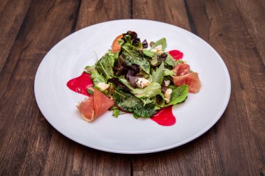 Beyaz tabakta kırmızı et carpaccio ve ahşap masada salata..