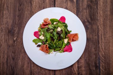 Beyaz tabakta kırmızı et carpaccio ve ahşap masada salata..