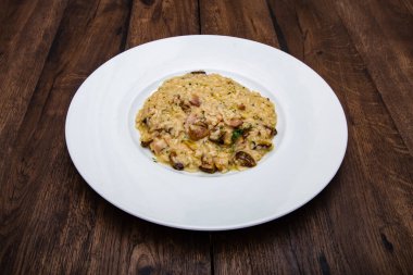 Porcini mantarlı İtalyan pilavı ve ahşap bir masada beyaz bir tabakta domuz pastırması..