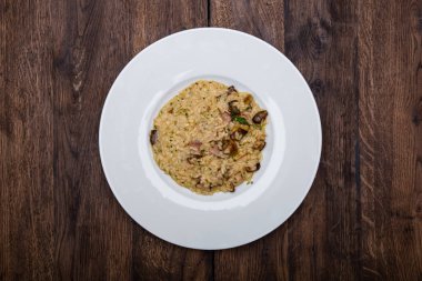 Porcini mantarlı İtalyan pilavı ve ahşap bir masada beyaz bir tabakta domuz pastırması..