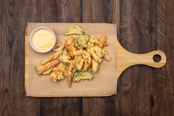 Tempura içinde sebzeler, ahşap bir tahtada sos ve parşömen..