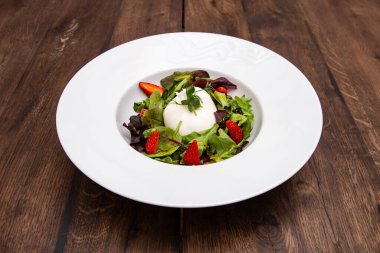 Taze İtalyan buratta peyniri karışık salata yaprakları ve ahşap bir masada bir tabakta çilek. İtalyan mutfağı.