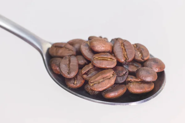 Grãos de café torrados em colher inoxidável no fundo branco spac — Fotografia de Stock