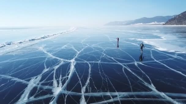 Pessoas passeio turístico ir na superfície lisa. Lago pitoresco Baikal rachaduras azul brilhante gelo claro hummocks neve snowdrifts. Melhor Norte da Rússia Ásia. Inverno dia ensolarado céu azul. Abordagem aérea . — Vídeo de Stock