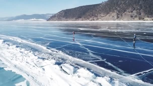 Los turistas caminan sobre una superficie lisa. Pintoresco lago Baikal Grietas azul brillante hielo claro hummocks nieve derrapes. Mejor Norte de Rusia Asia. Invierno día soleado cielo azul. Enfoque aéreo . — Vídeos de Stock