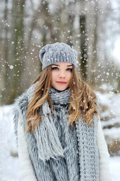 Menina bonita com cabelos longos encaracolados em cachecol de malha na floresta de inverno sob flocos de neve . — Fotografia de Stock