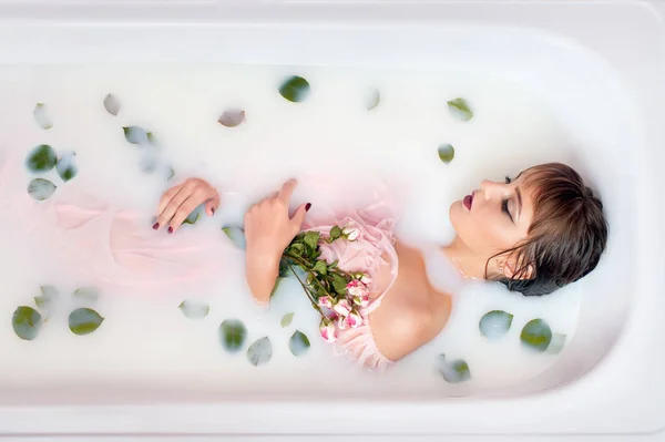 젊은 여 자가 우유 및 장미 꽃잎 목욕. — 스톡 사진