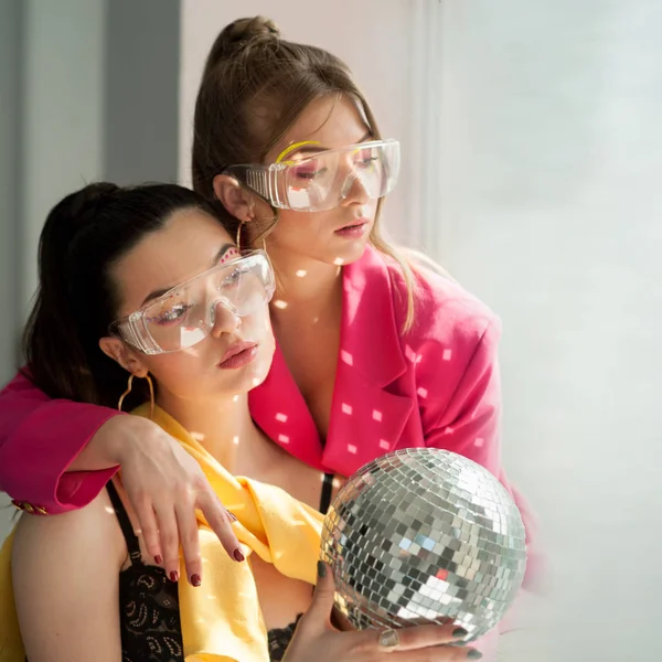 Jeunes femmes avec un maquillage d'épice coloré lumineux et boule disco miroir avec brille sur le corps de shes près de la fenêtre — Photo