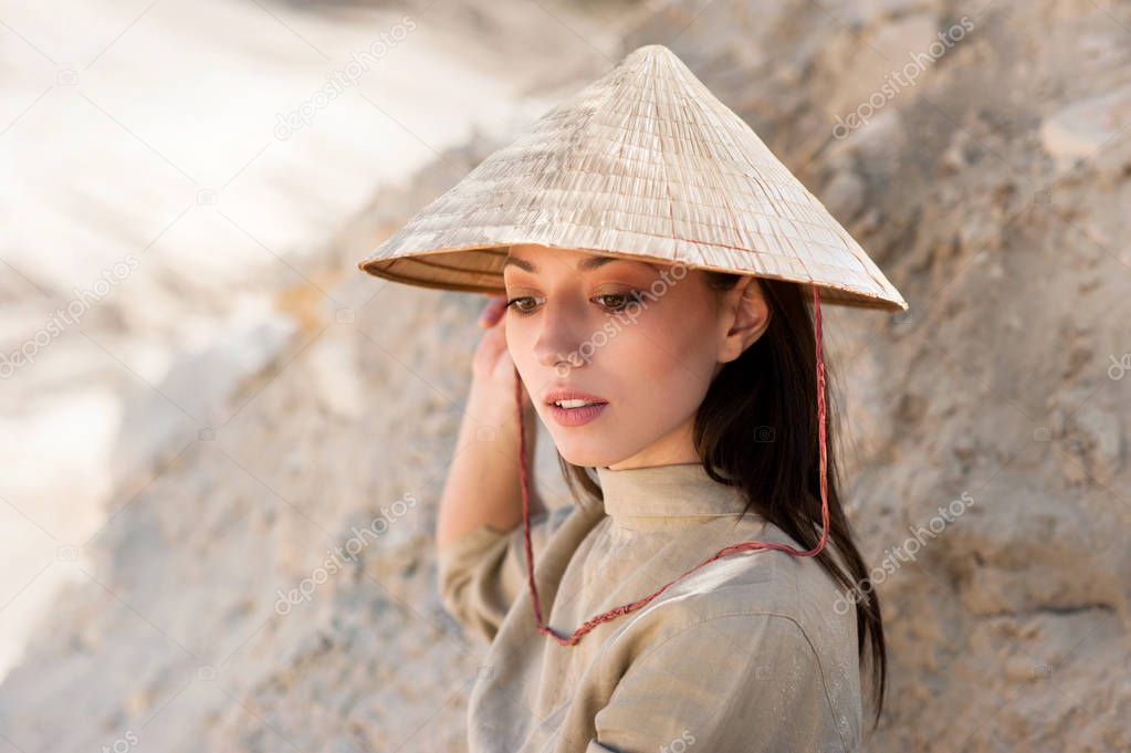 eastern oriental appearance girl in khaki dress and vietnamese hat on sand