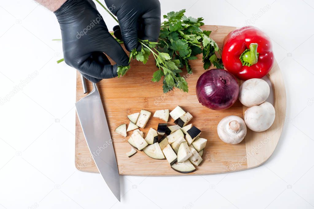 chef in black gloves slices eggplant on bamboo board above