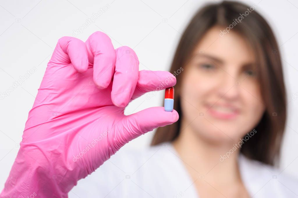 female doctor with pink latex gloves holding pills on white background. Focus on pill