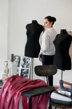 Tasarımcı - terzi atölyesinde mankenlerle duruyor