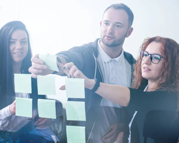 Office team work, people discussing in front of glass wall using post it notes and stickers at startup